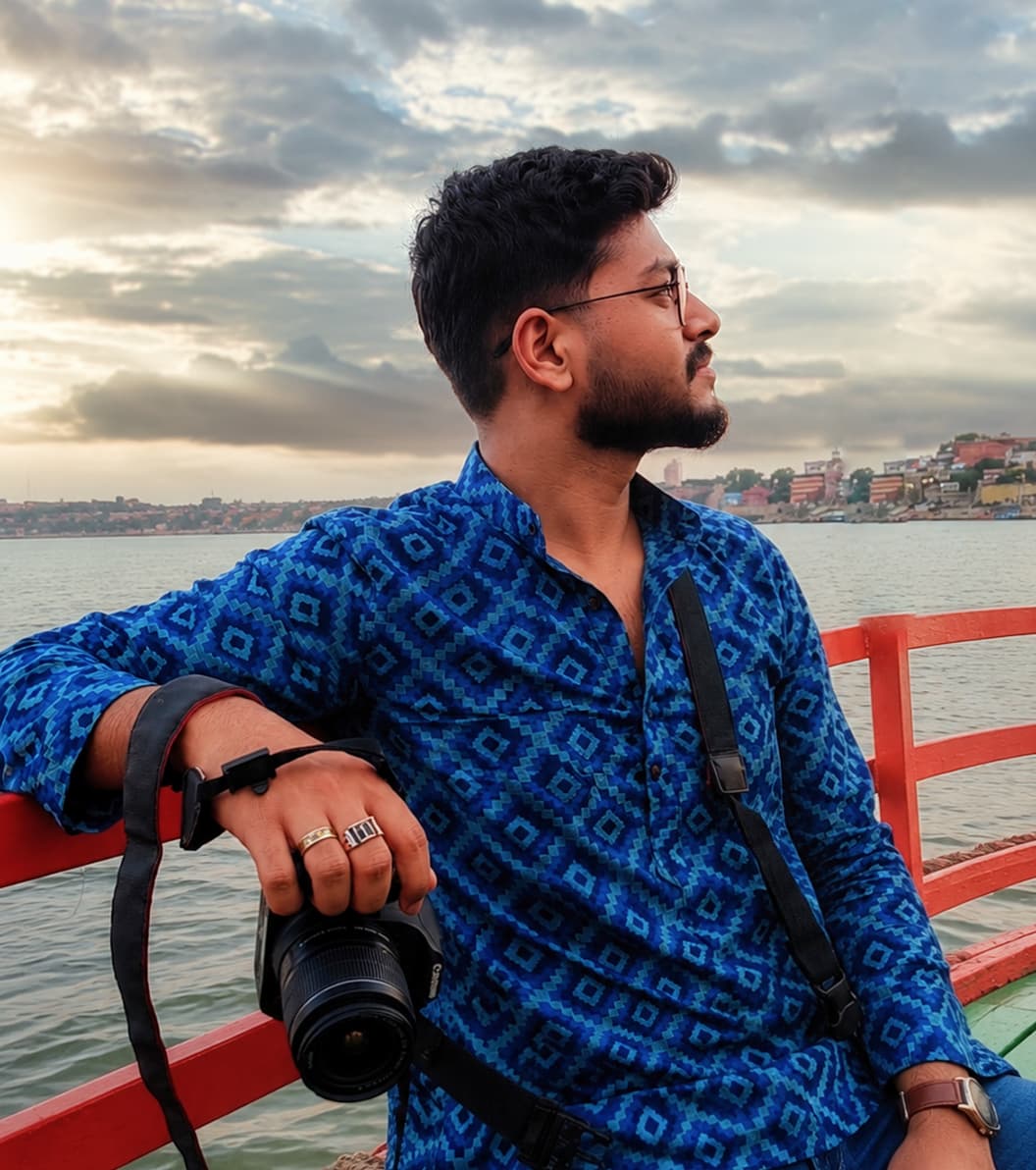 Harsh holding a camera on a boat at sunset, overlooking a riverside town