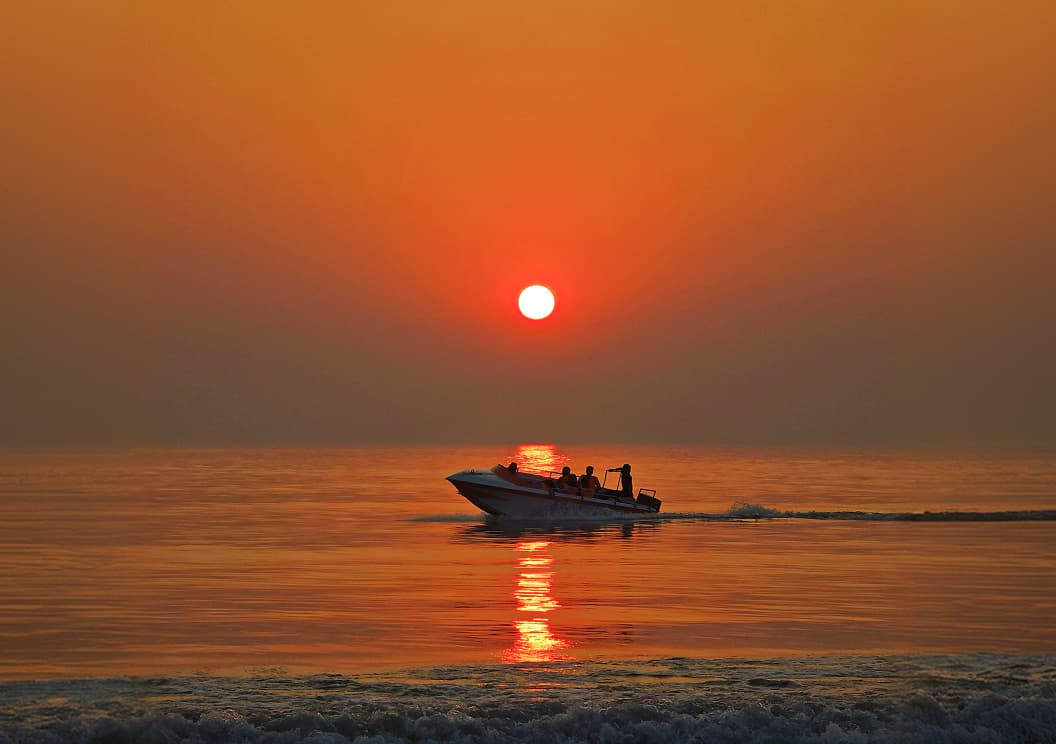 A boat silhouetted against a red sunset over the ocean